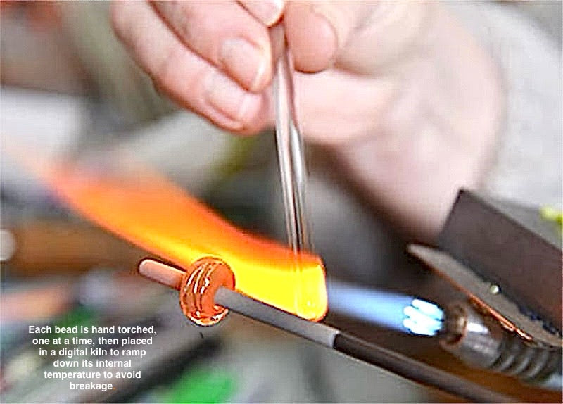 Hand holding a metal rod with a flame source, likely for heating purposes.