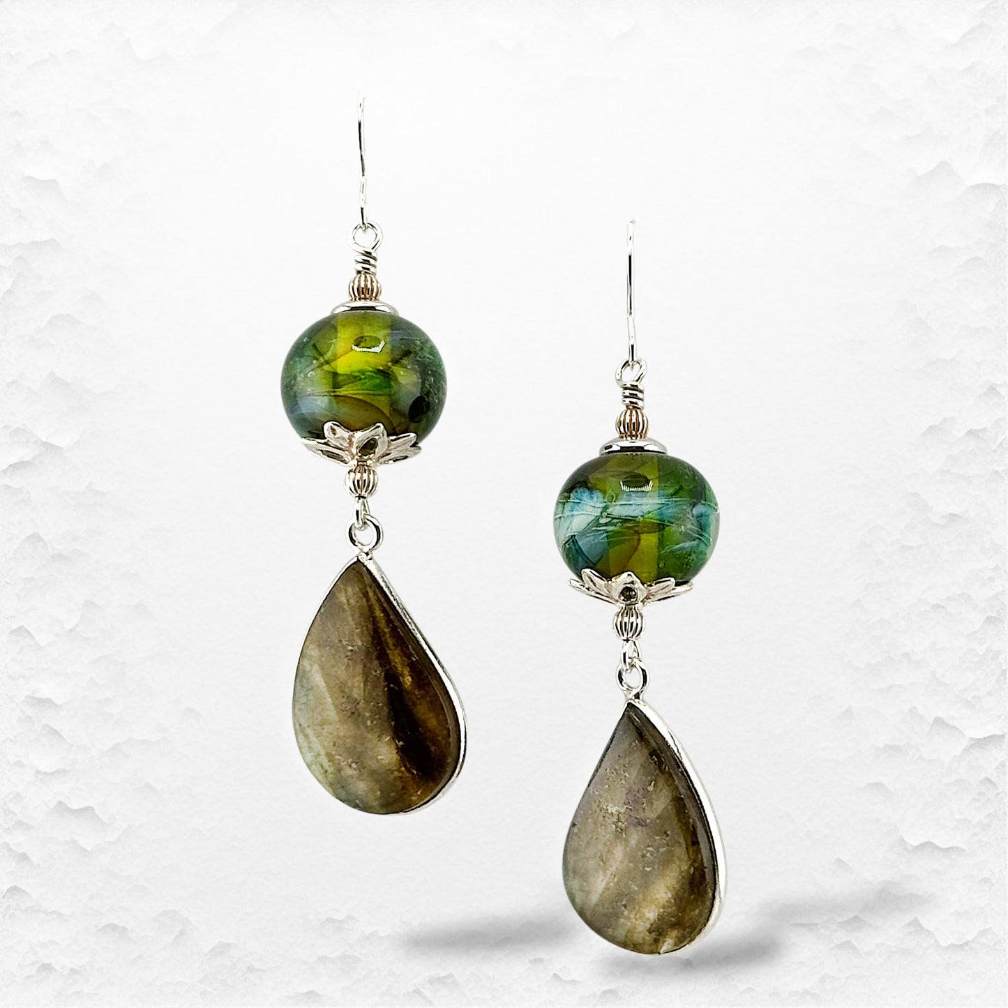 Pair of earrings with green beads and teardrop-shaped stones on a textured white background