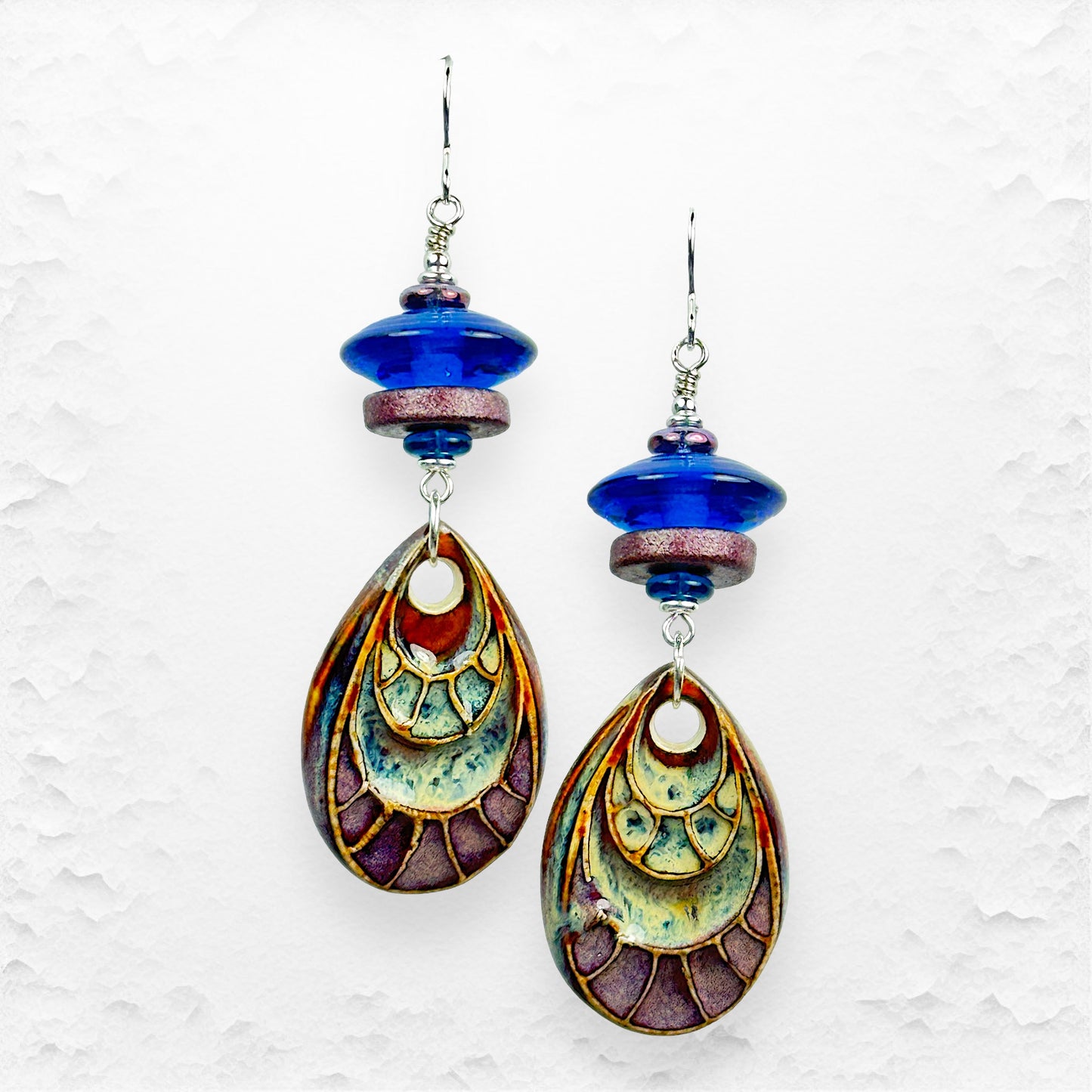 Colorful ceramic teardrop earrings with blue accents on a textured white background