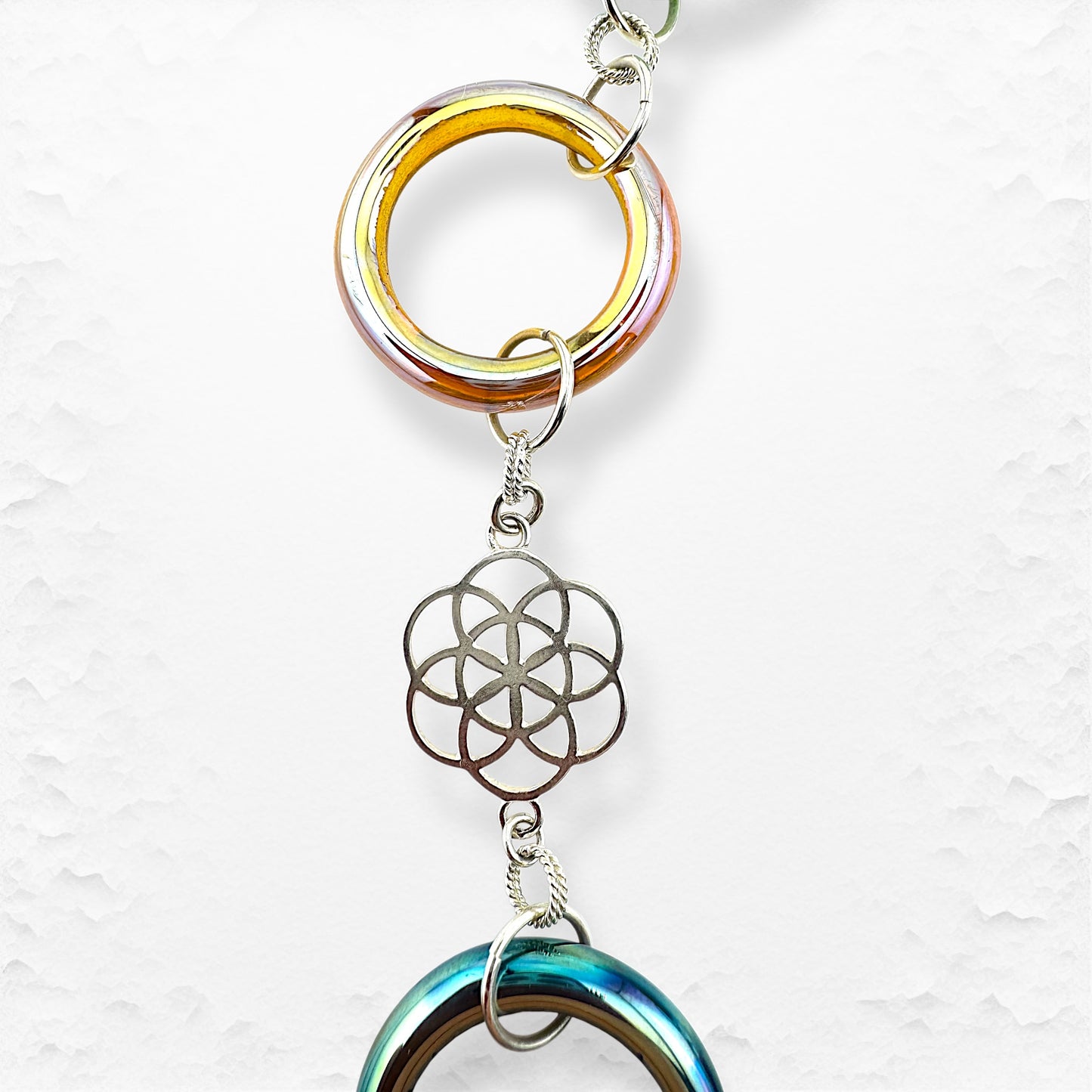 Decorative chain with colorful rings and a metal flower-shaped pendant on a light gray background