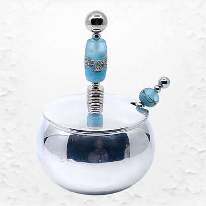 A handcrafted glass beaded sugar bowl with a stainless steel spoon, featuring a blue glass bead design and a silver-colored metal rim.