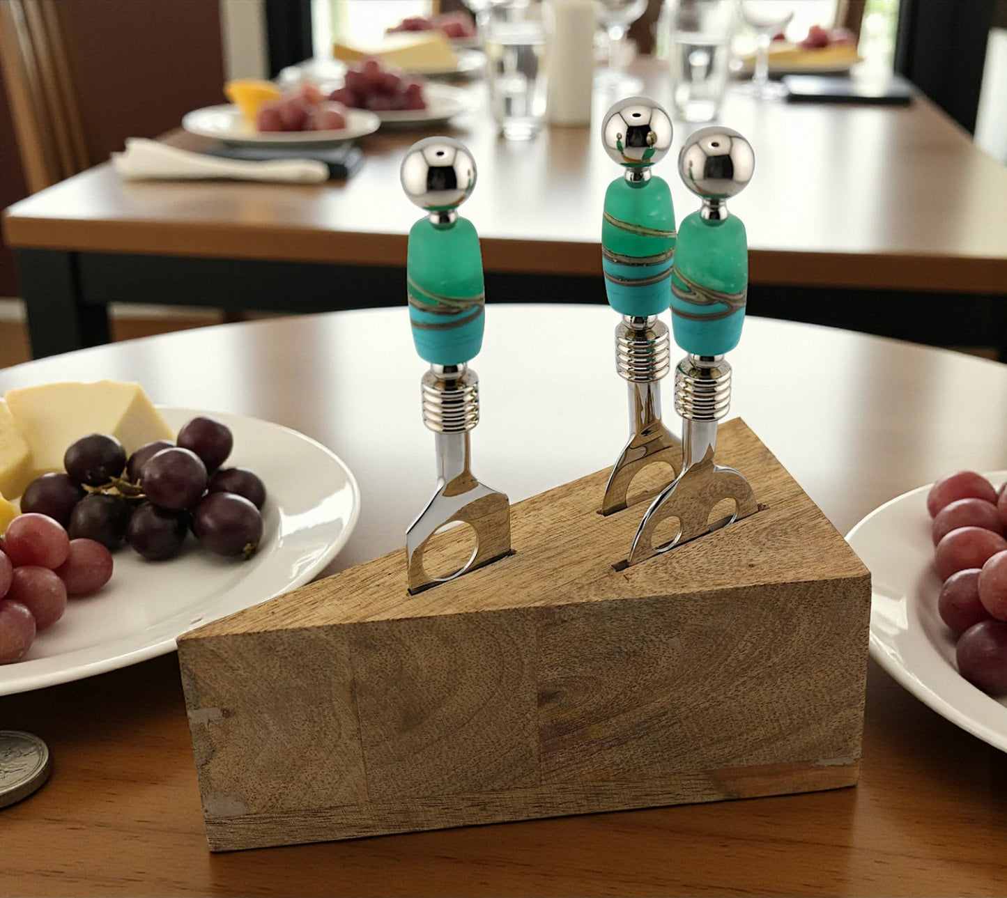 Two cheese forks with turquoise handles on a wooden block, set against a dining table background.