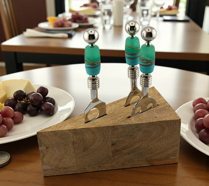 Two cheese forks with turquoise handles on a wooden block, set against a dining table background.