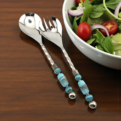 Silver salad servers with turquoise beads on a wooden table next to a bowl of salad.