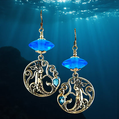 Mermaid-themed earrings with blue gemstones against an underwater background