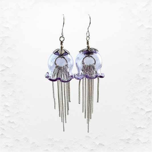 A pair of jellyfish-shaped dangling earrings made from clear glass with purple accents and silver-toned wire tentacles.