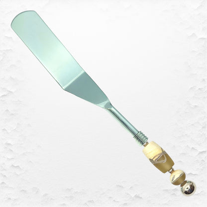 A stainless steel quiche or pastry server with a handle adorned by handcrafted glass beads in a turquoise color.