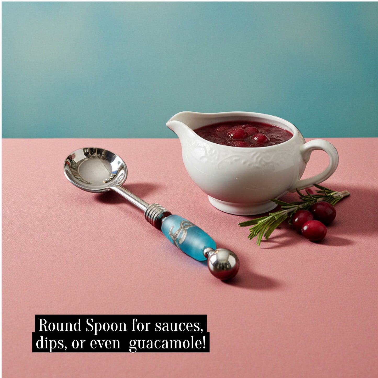 White sauceboat with red sauce, a decorative spoon, and cranberries on a pink surface with a teal background.
