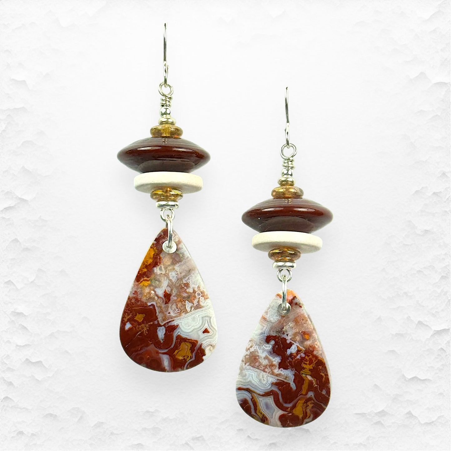 Pair of earrings with teardrop-shaped agate stones on a textured white background