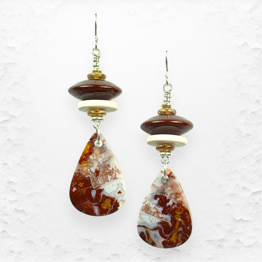 Pair of earrings with teardrop-shaped agate stones on a textured white background