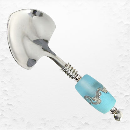 A stainless steel spoon with a small heart-shaped adorned with a turquoise handcrafted glass bead embellishment along the handle.