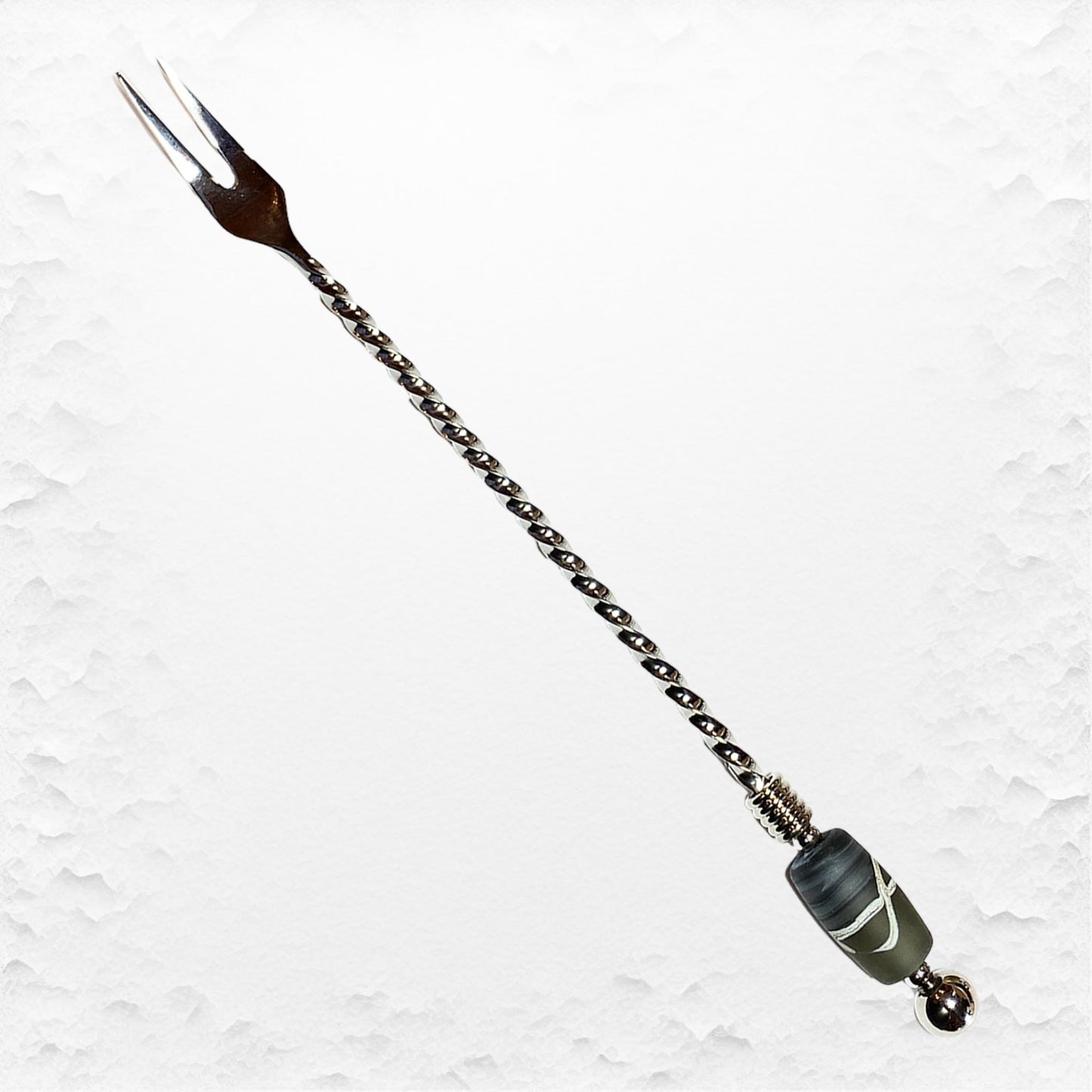 A long stainless steel pickle fork with a hand-torched glass bead design on the handle, featuring a brown handle and a green glass bead near the tip.
